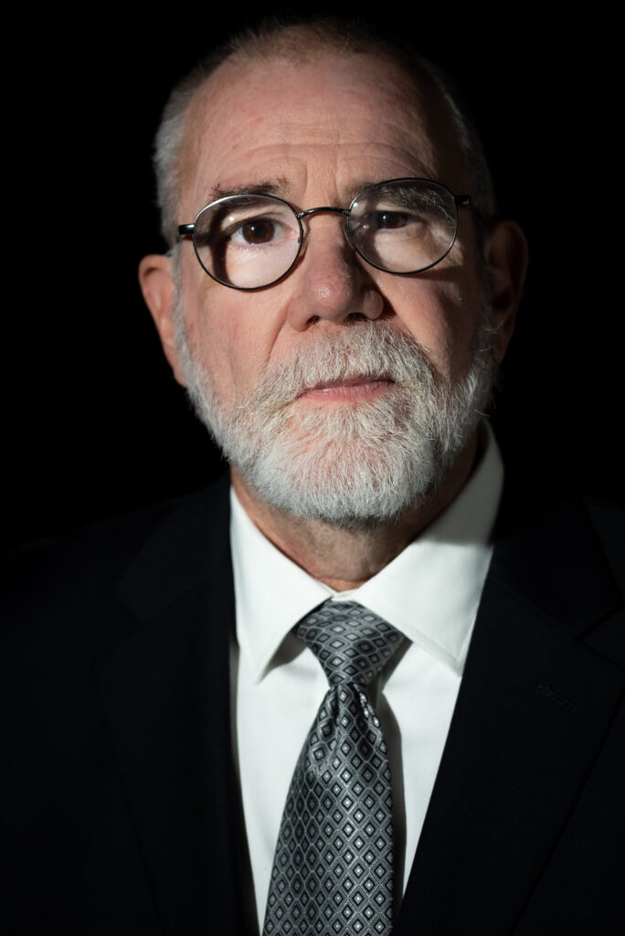 A man with glasses and a beard teaching in front of a whiteboard.